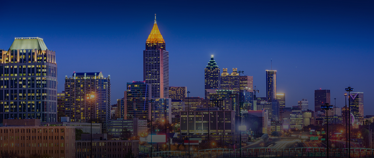 Nighttime skyline view of a brightly lit city with tall buildings and a clear sky.